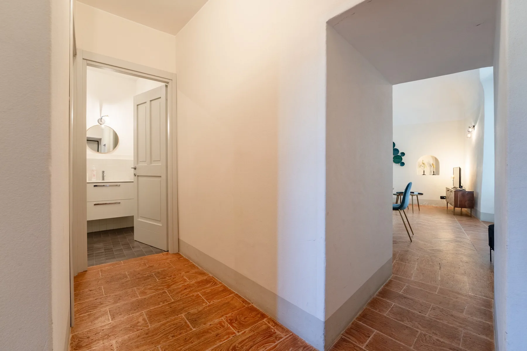Un pasillo de baldosas conecta un baño con una luminosa zona de estar.