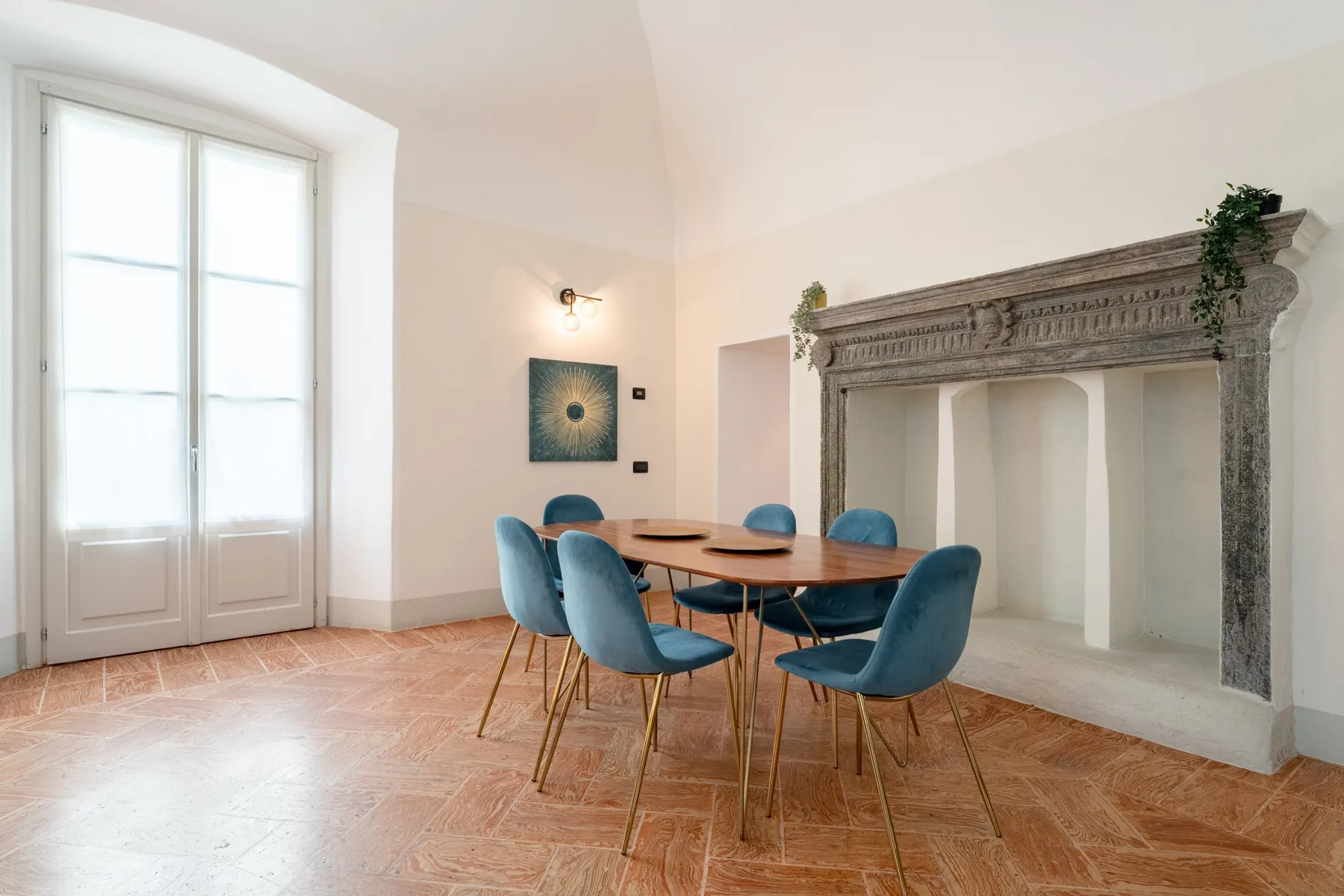 Comedor con una mesa de madera y asientos azules junto a una gran chimenea.