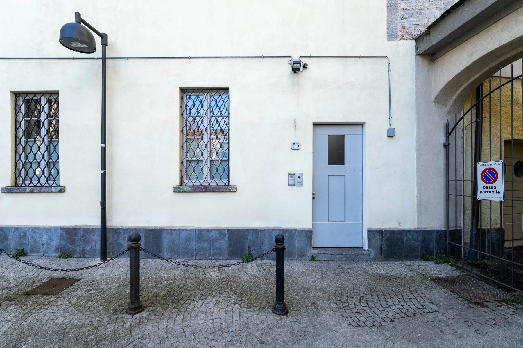 Una fachada clara con ventanas enrejadas y una puerta de entrada azul grisácea.