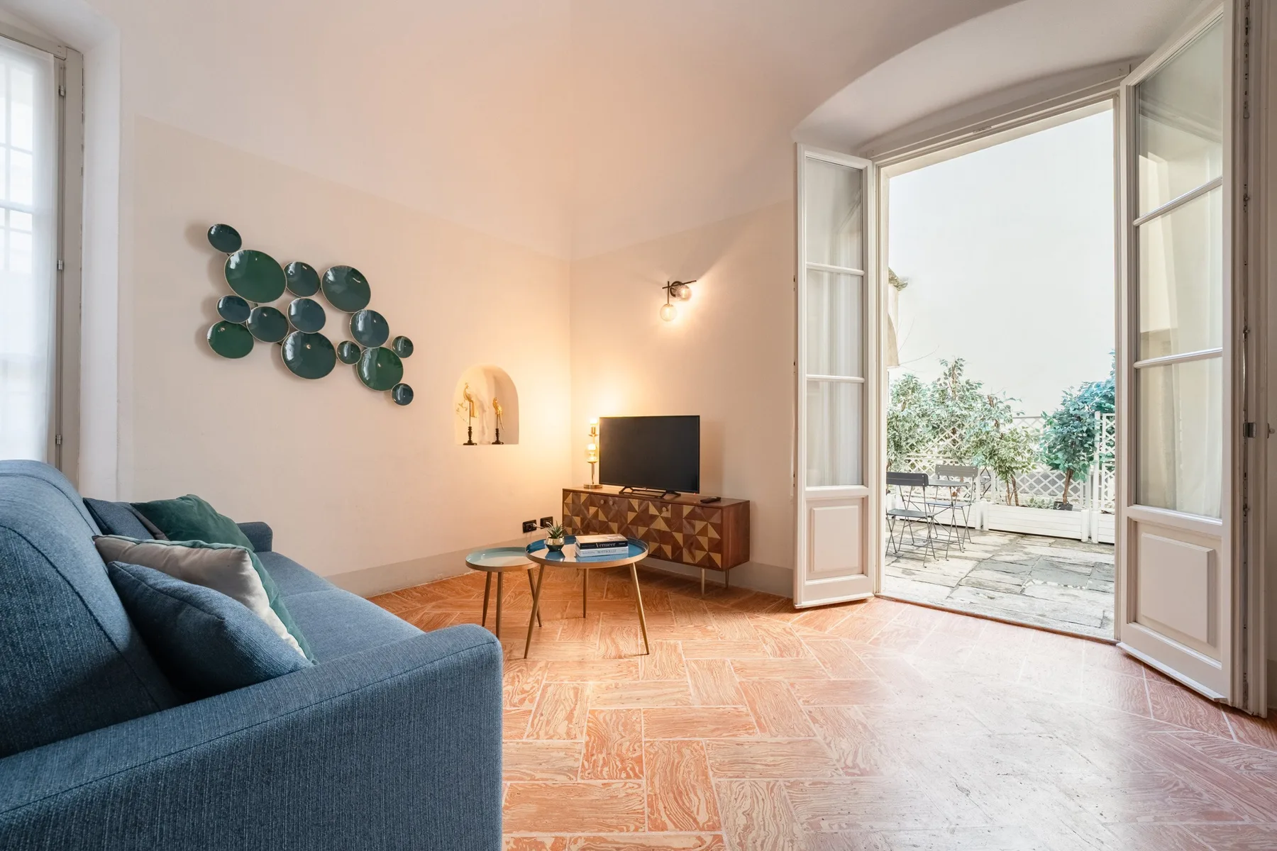 Una sala de estar con asientos azules, un televisor y puertas abiertas a una terraza.