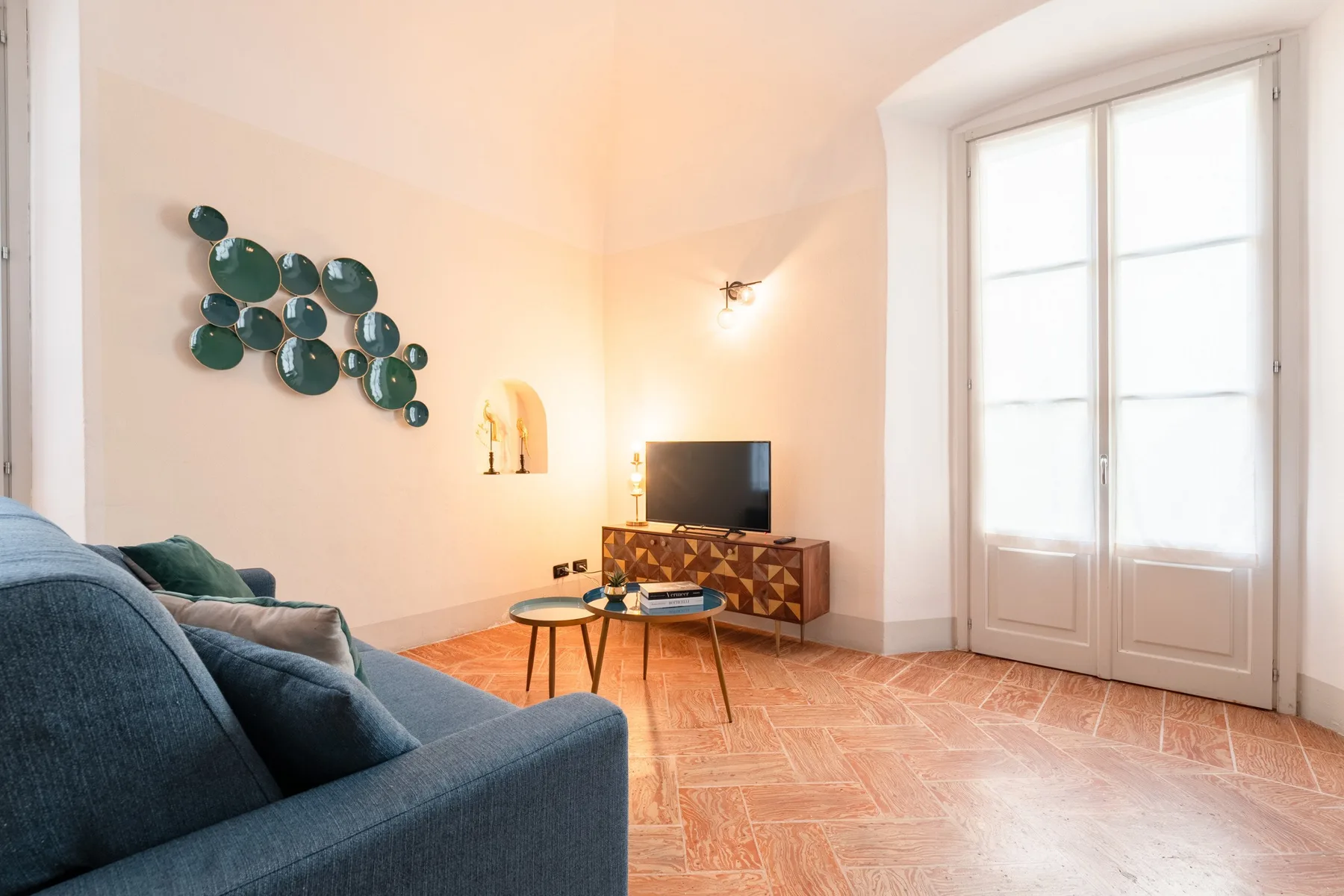 Una sala de estar luminosa con asientos, un televisor y puertas dobles altas.