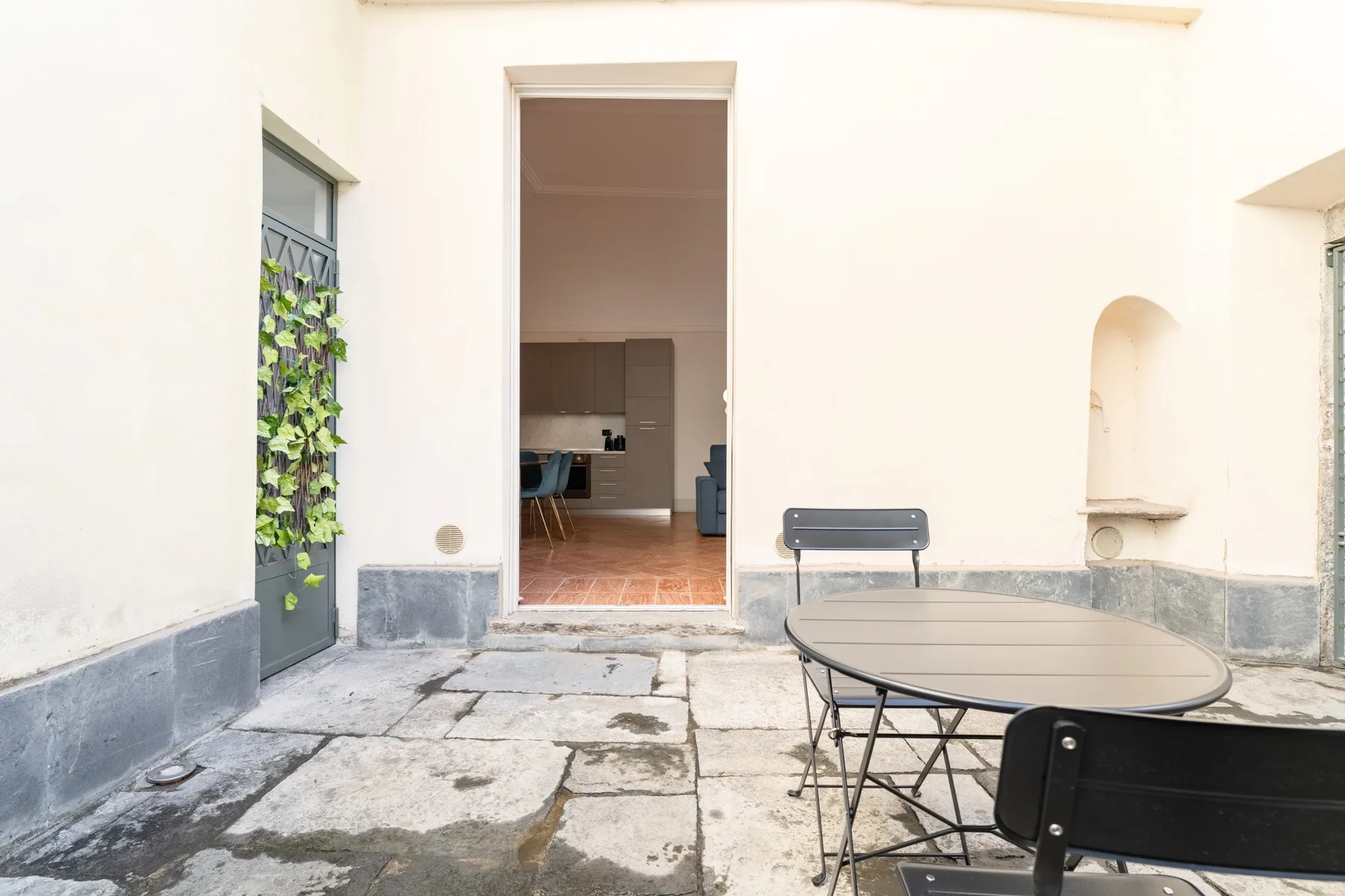 Un pequeño patio exterior con una mesa y asientos junto a una puerta abierta.