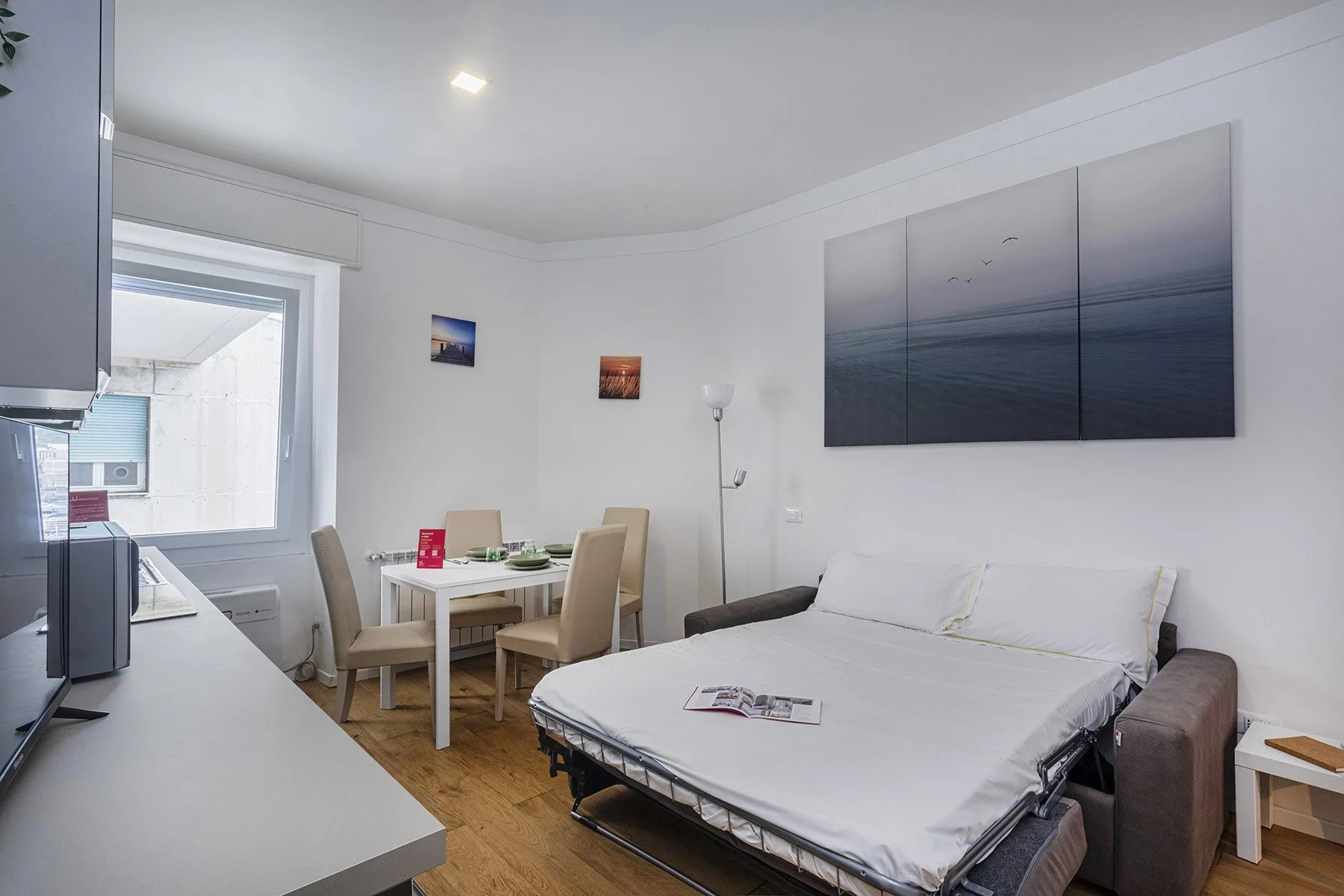 A compact bedroom with a bed, dining table, and wall art.