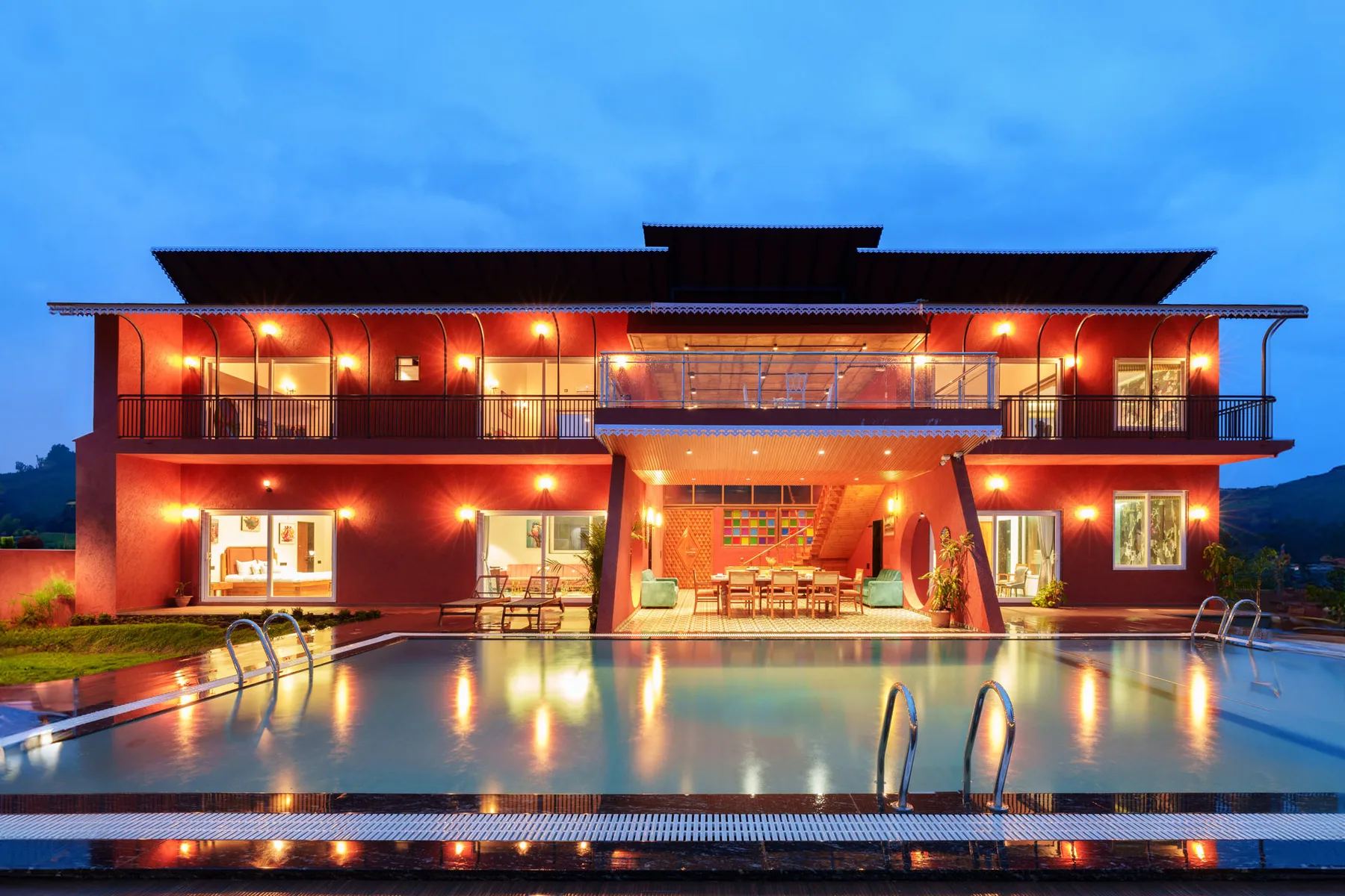 Una casa moderna da a una piscina, con luces cálidas que iluminan la fachada.