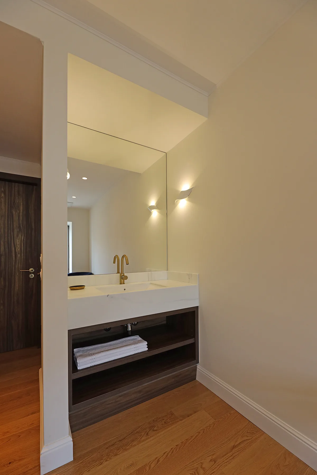 Un lavabo de baño con un espejo amplio y un estante abierto oscuro.