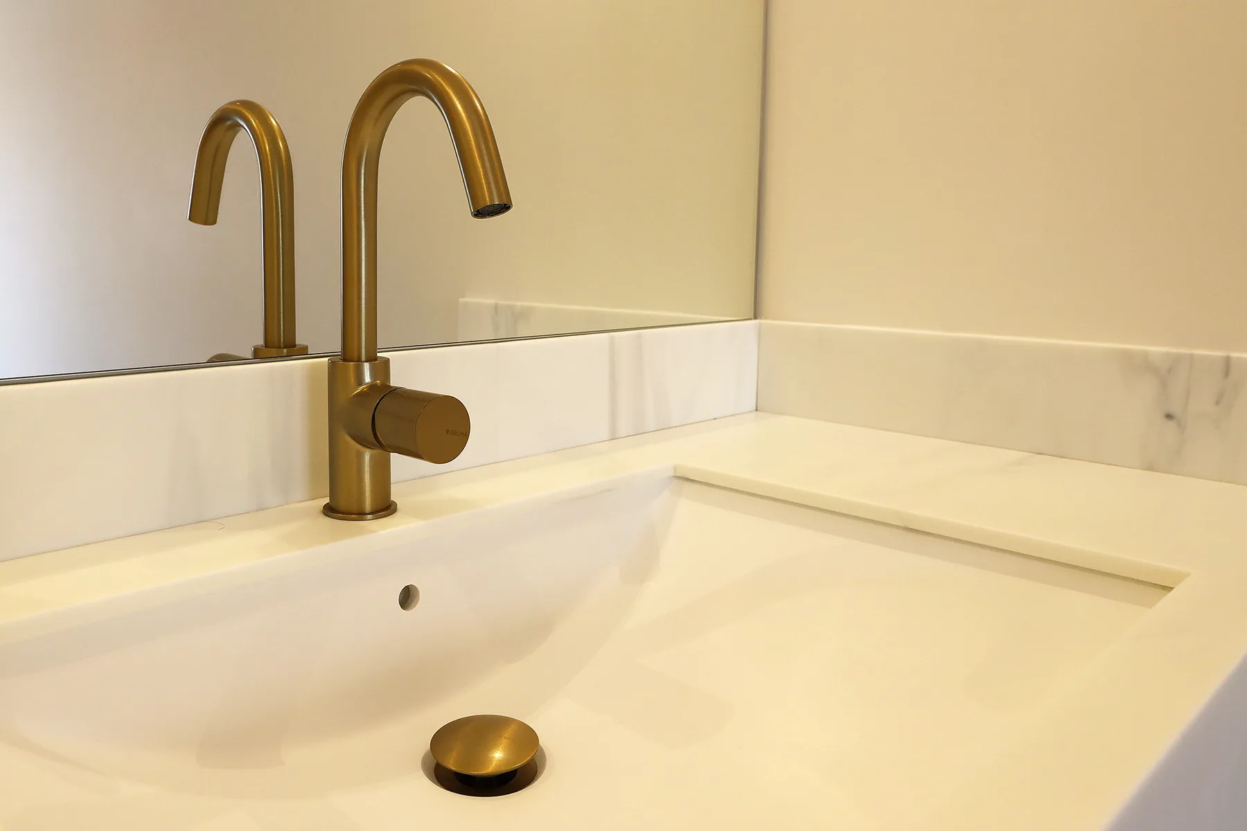 Un lavabo con grifo de color latón está situado bajo un espejo.