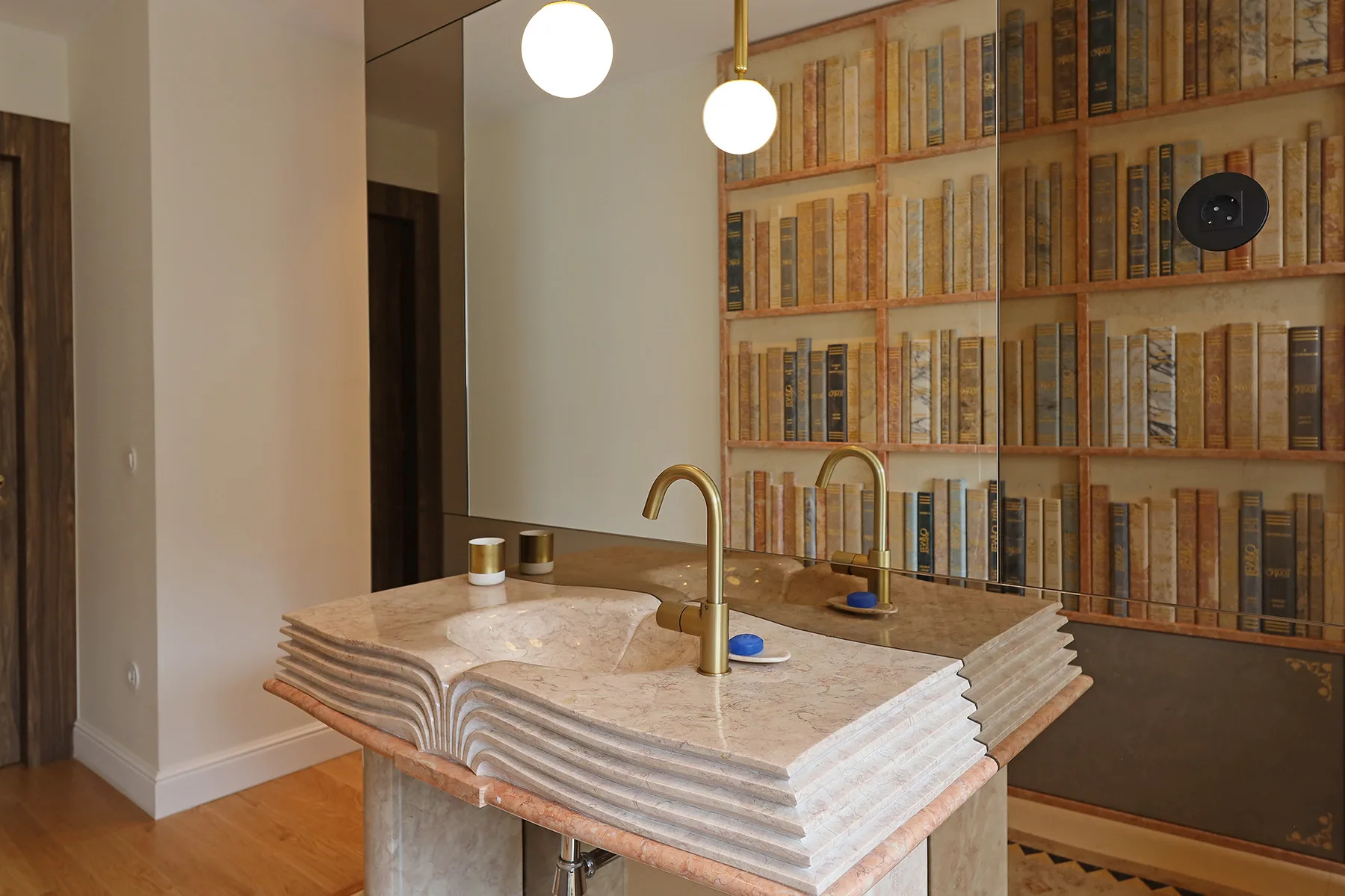A bathroom vanity with two faucets stands before a wall of bookshelves.