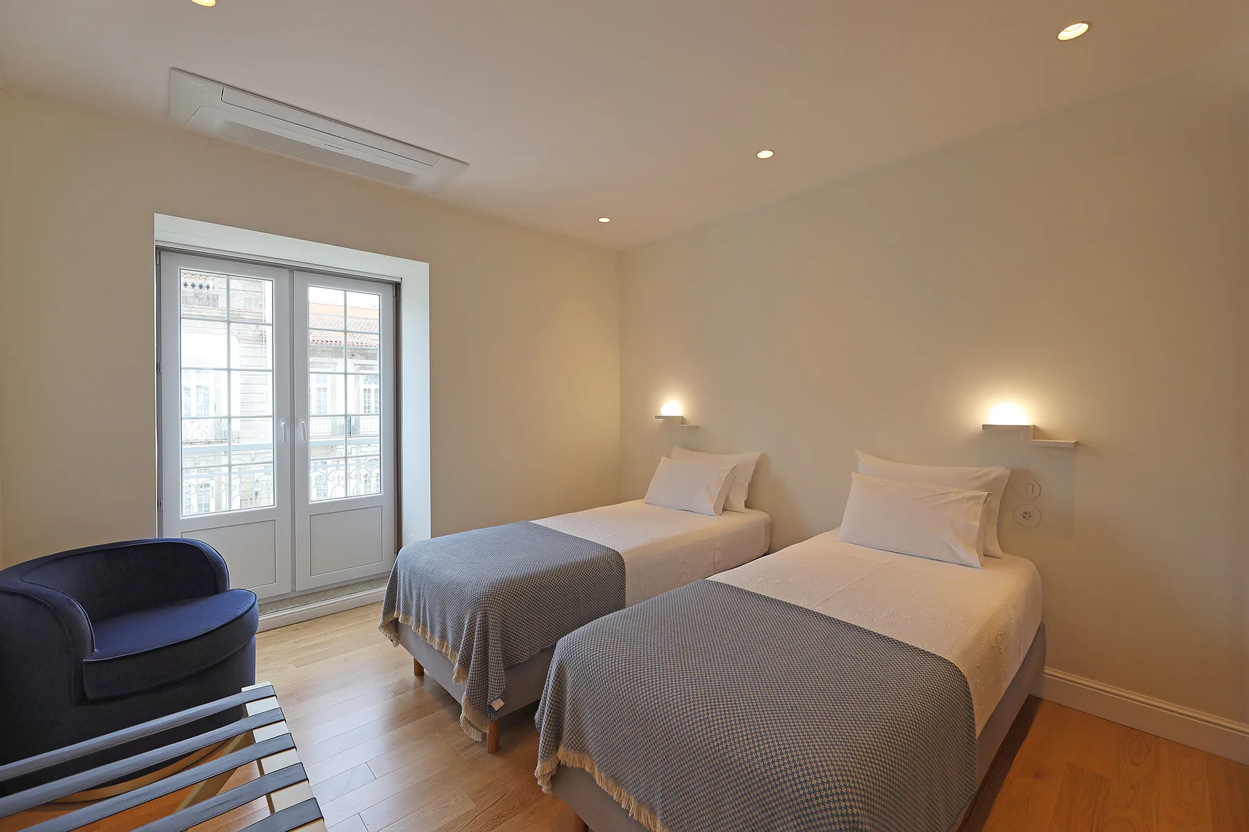 Dormitorio con dos camas, una ventana y un sillón azul.