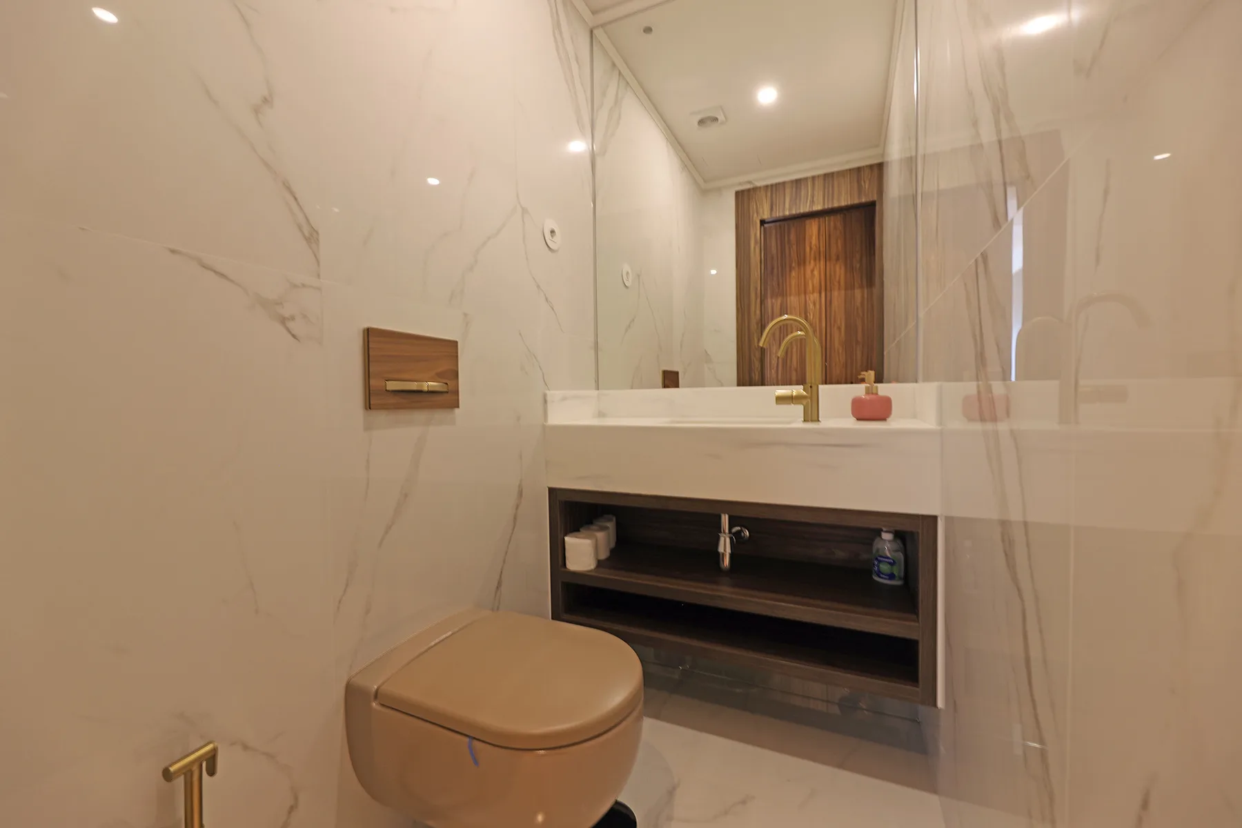 Un baño con un inodoro suspendido y un lavabo bajo un espejo grande.