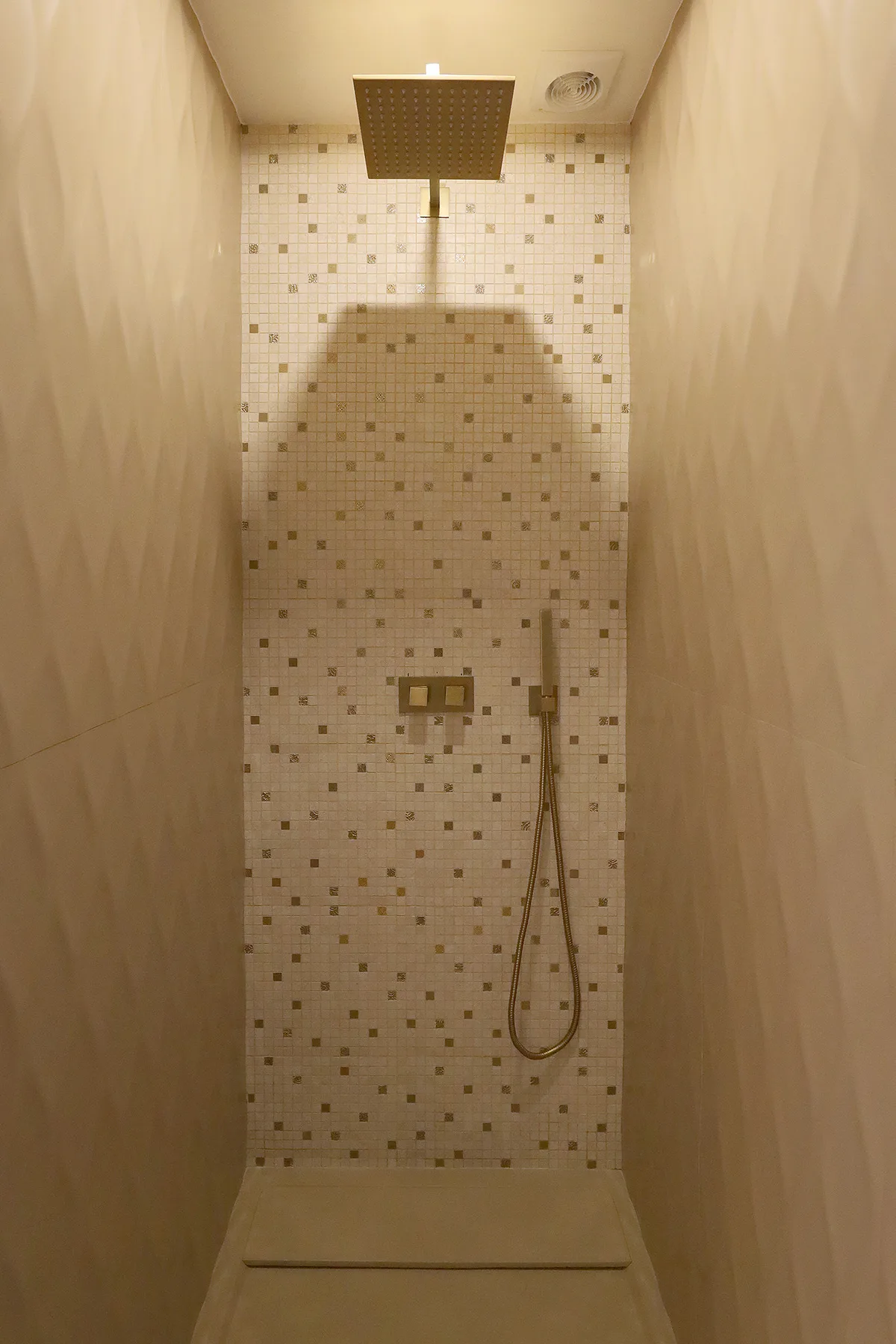 Una zona de ducha con azulejos, rociador cuadrado y ducha de mano.