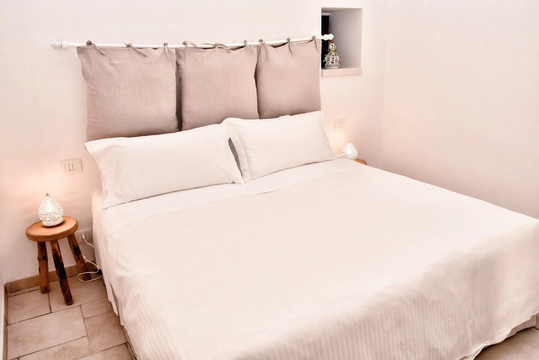 A bright bedroom features a neatly made bed with soft neutral bedding.