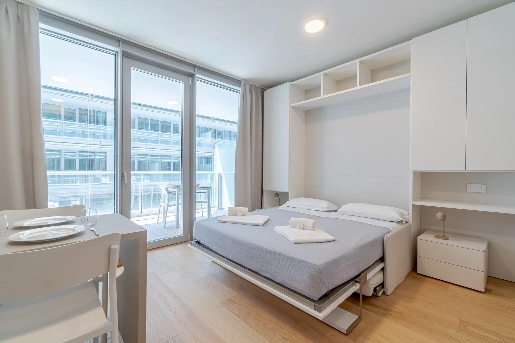 A bright bedroom with a bed beside large windows and built-in shelving.