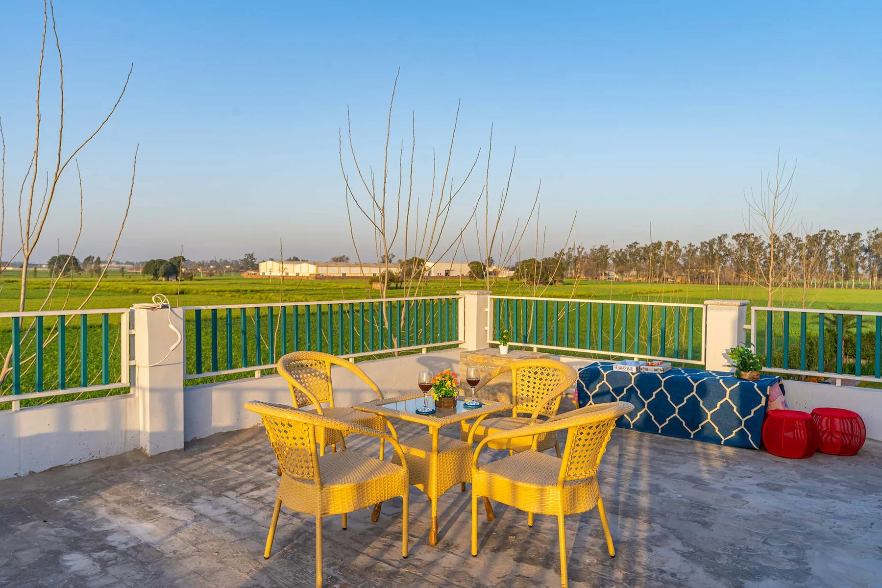 Una terraza al aire libre con asientos amarillos y una mesa da a campos verdes.