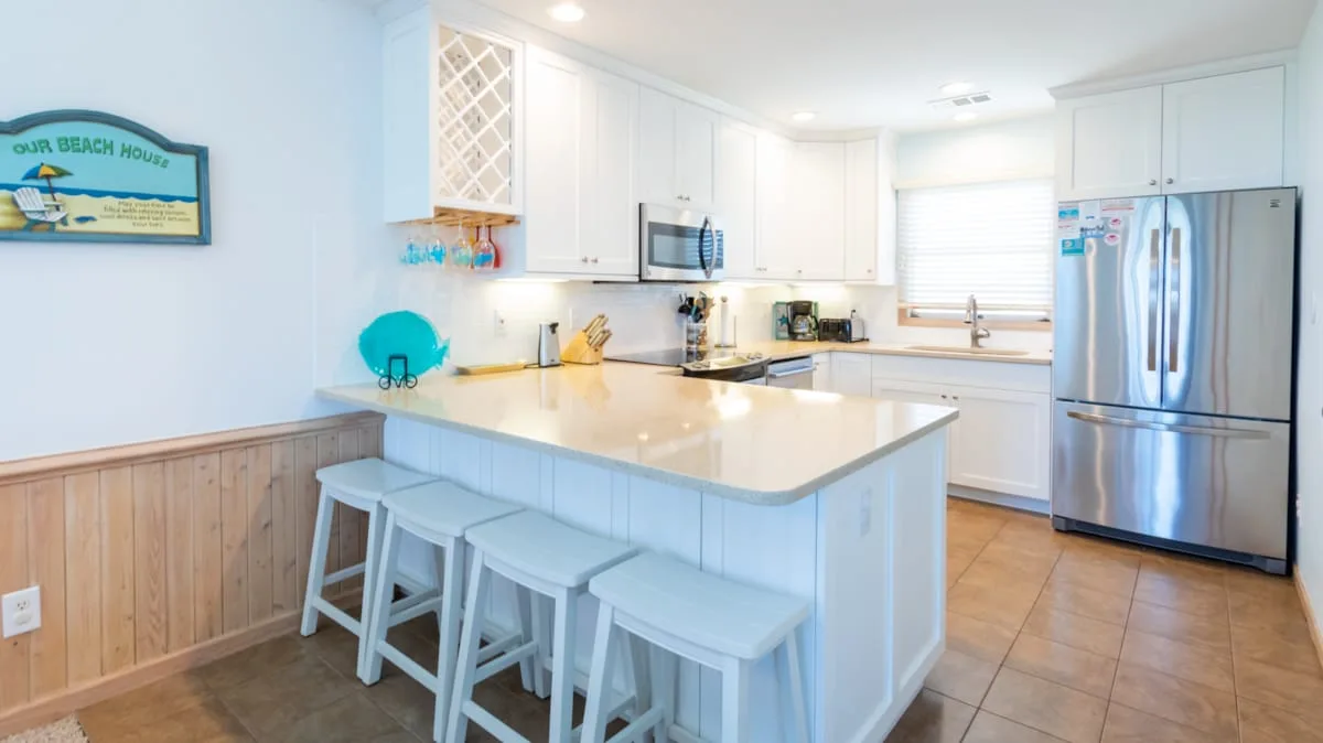 Una cocina luminosa con gabinetes blancos y una isla grande con asientos.