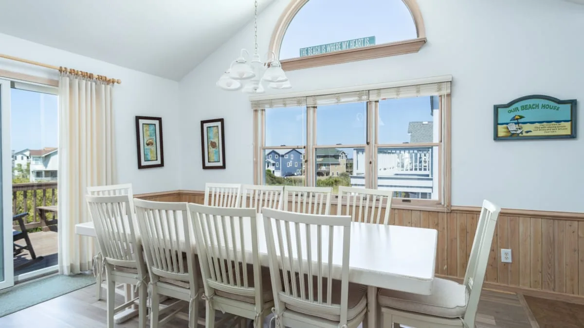Un comedor luminoso con una mesa larga y sillas blancas junto a grandes ventanas.