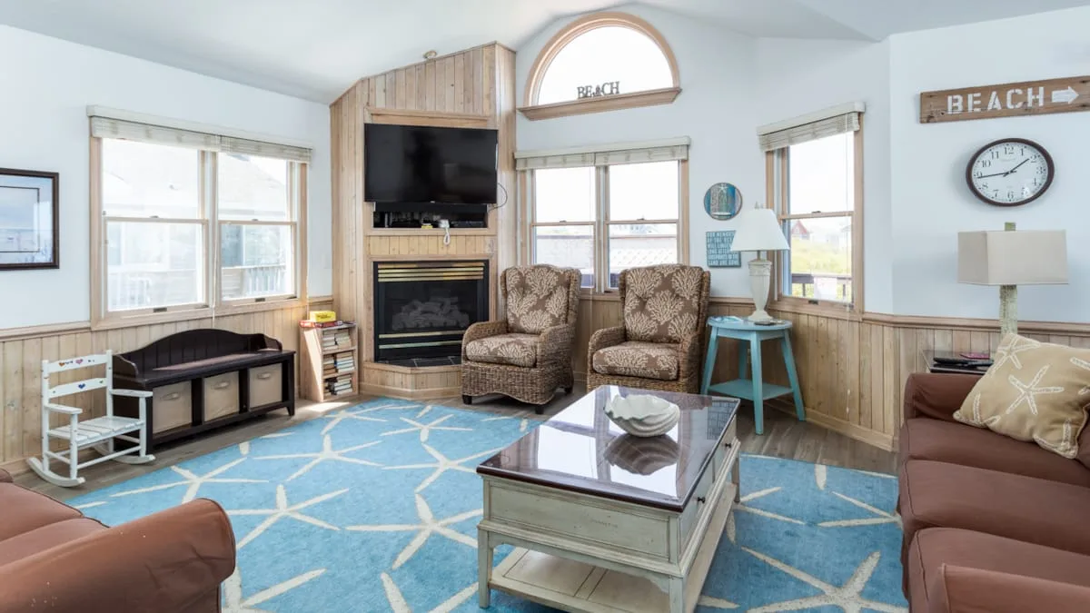 A bright living room has cushioned seating, a glass coffee table, and large windows.