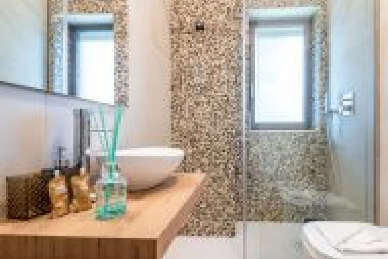 Un baño con lavabo sobre encimera, paredes de mosaico y ducha de vidrio.