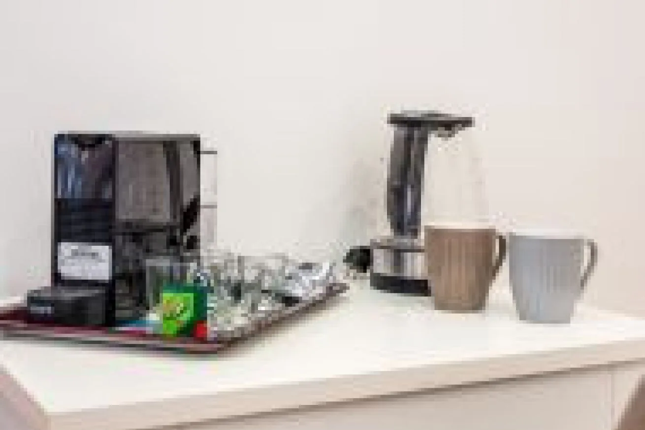Una estación de bebidas con cafetera, tazas y suministros sobre una encimera.