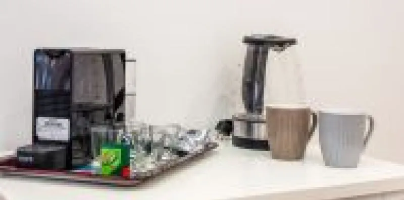 Una estación de café sobre la encimera con cafetera, tazas y vasos.