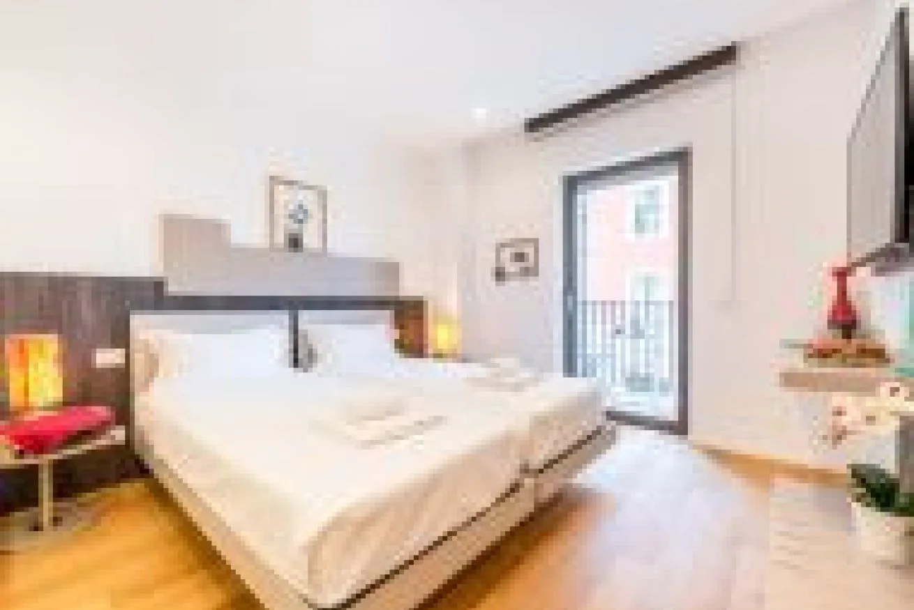 Un dormitorio luminoso con una cama grande y una puerta de vidrio que da a un balcón.