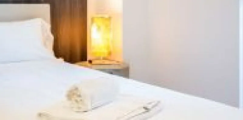 A bedroom with white bedding and a lit bedside lamp.