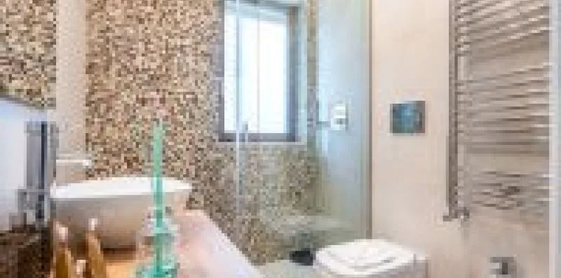 Un baño con azulejos, lavabo, zona de ducha y ventana.
