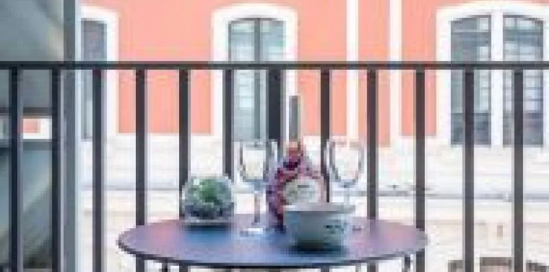 A balcony seating area with a round table overlooks a coral-colored building.