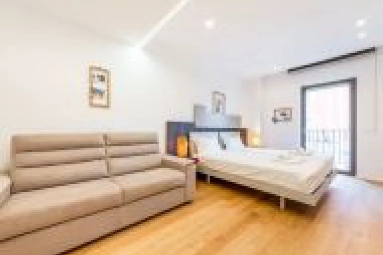 Un dormitorio luminoso con una cama grande, asientos acolchados y una puerta al balcón.