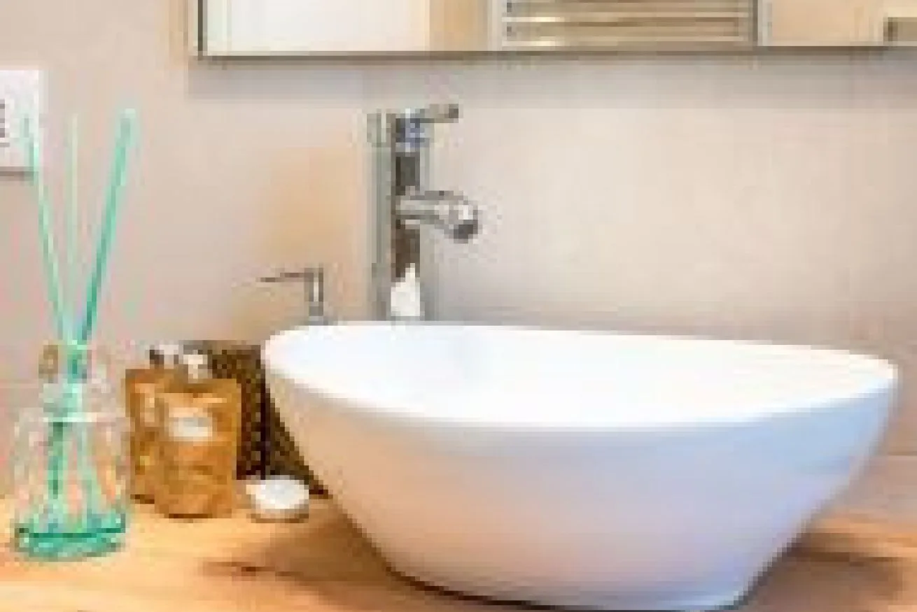 Un tocador de baño presenta un lavabo blanco sobre encimera y un grifo cromado.