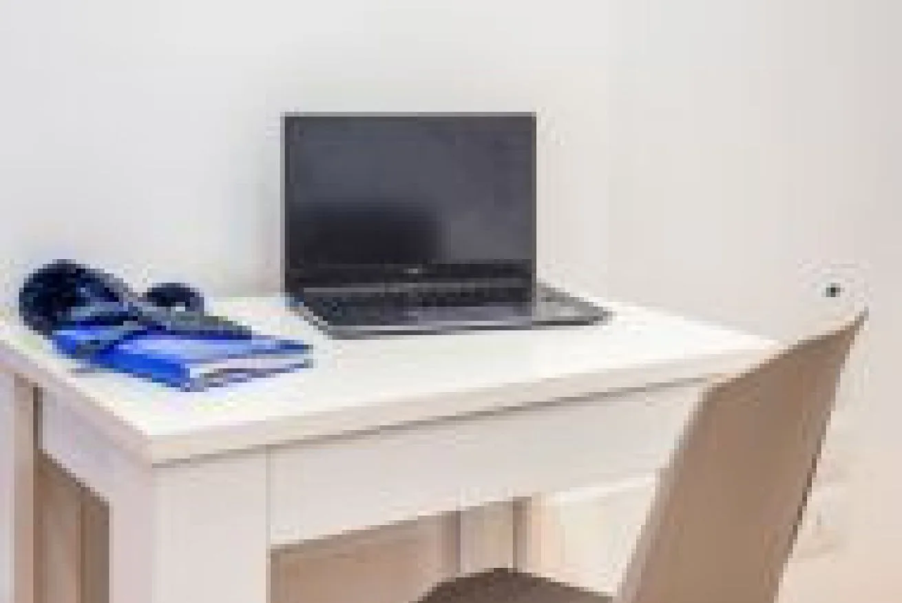 Un escritorio con una computadora portátil abierta y papeles está junto a una silla.