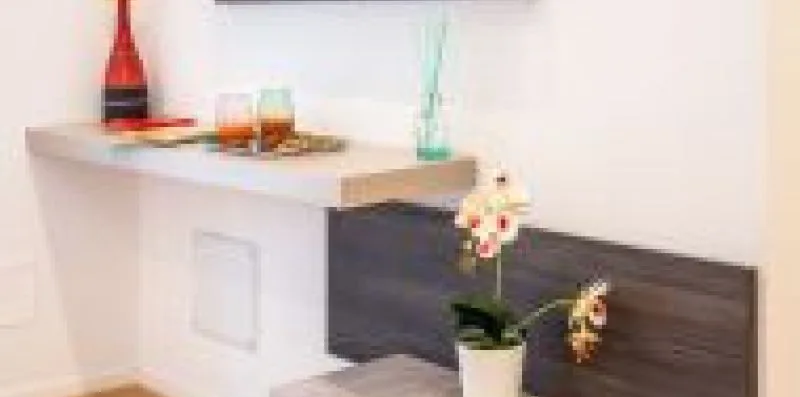A white countertop with decorative bottles and flowers sits above a dark wood panel.