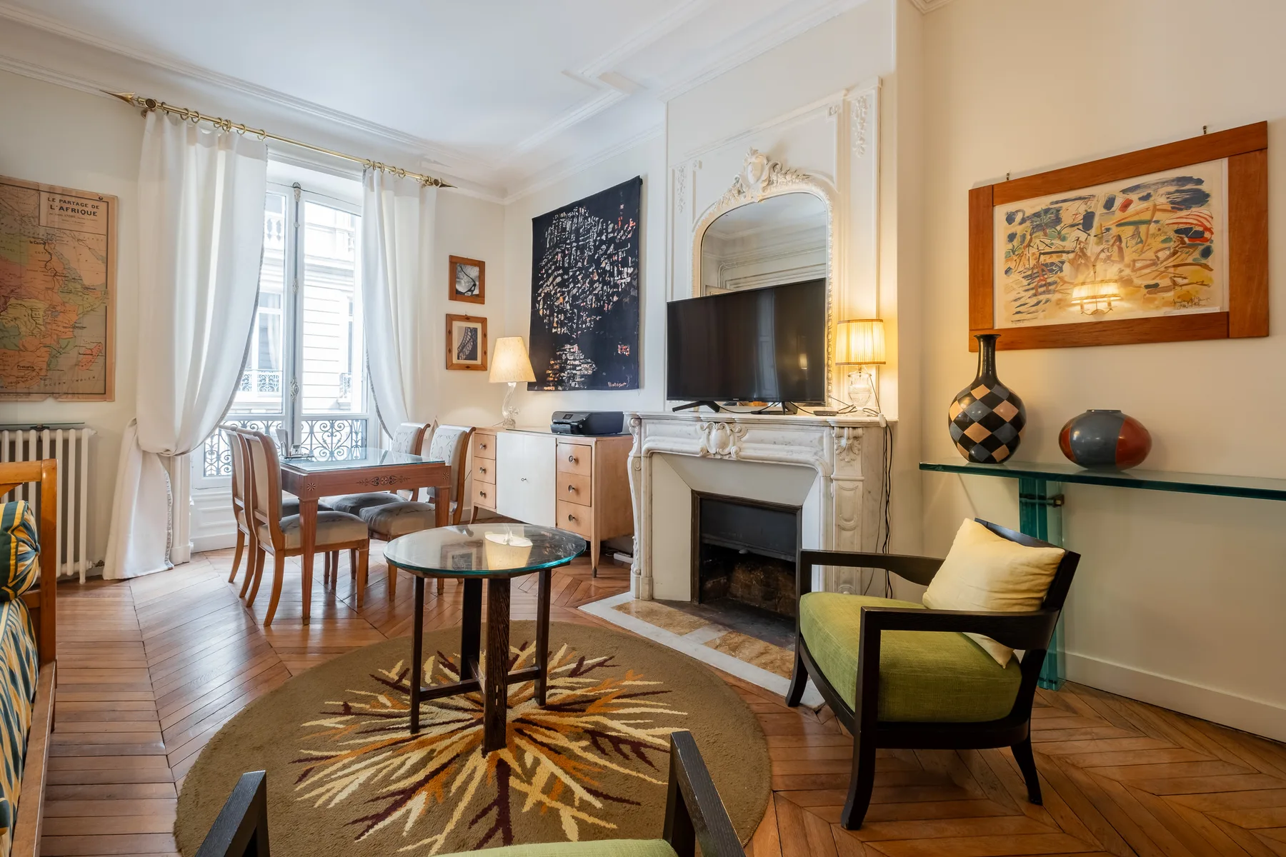 A bright living room with a fireplace, seating, and a dining area by tall windows.