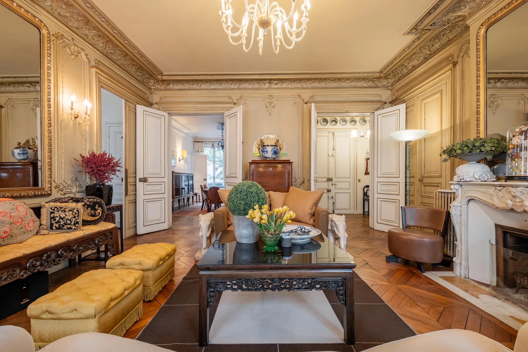 An ornate living room features decorative wall panels and seating around a central table.