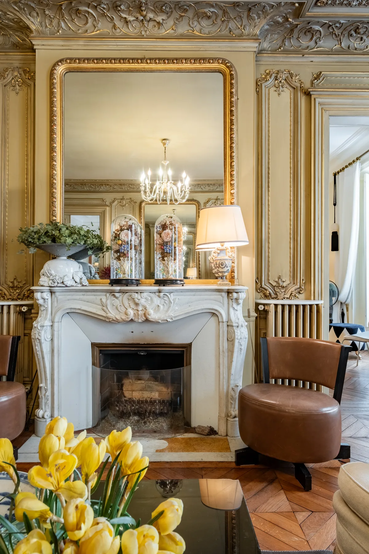 An ornate living room centers on a marble fireplace beneath a large mirror.