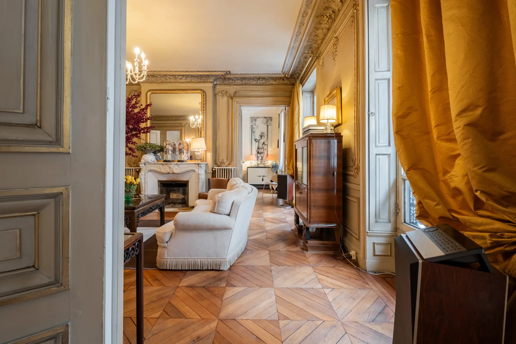 An ornate living room with seating, a fireplace, and a patterned wood floor.