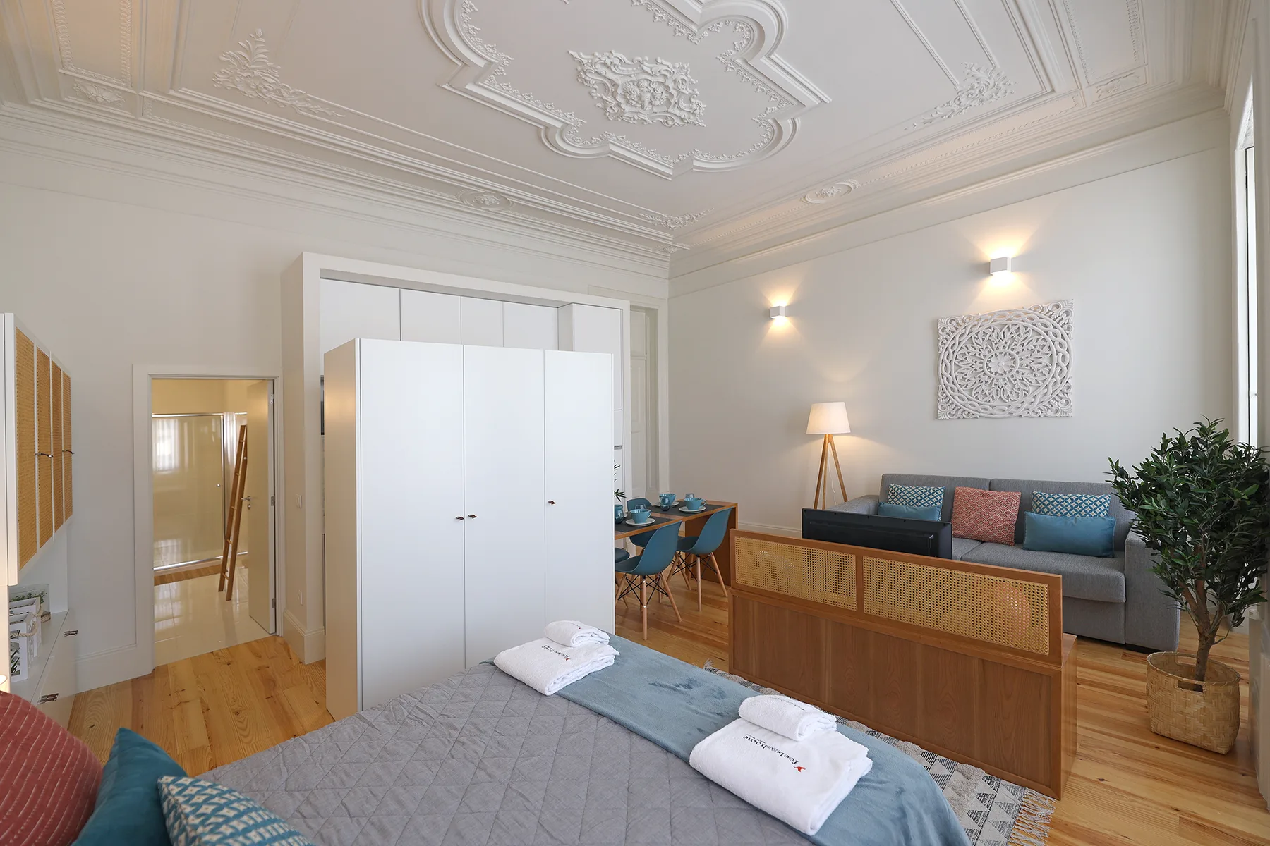 A bright studio room with a bed, seating area, and decorative ceiling.