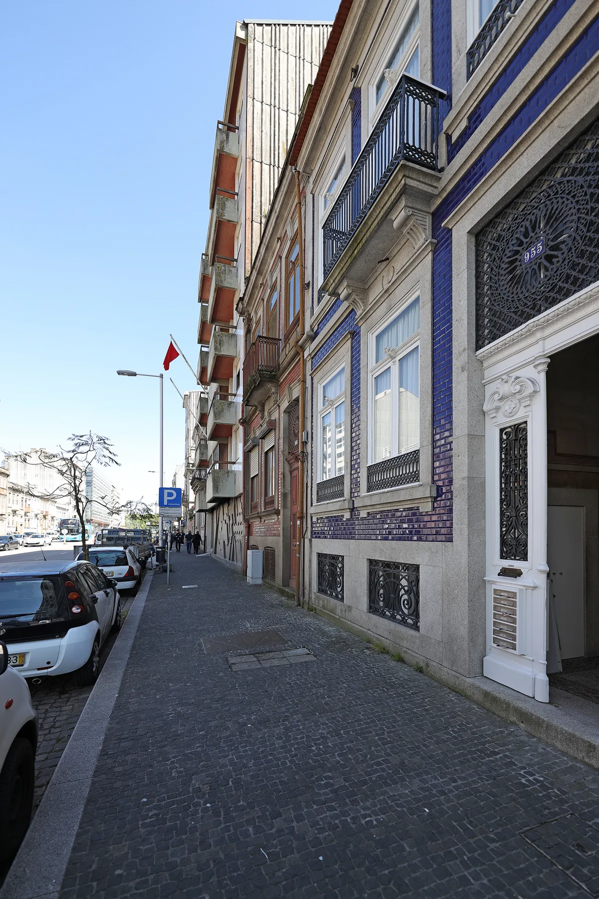 A cobbled city street lined with parked cars and ornate building façades.
