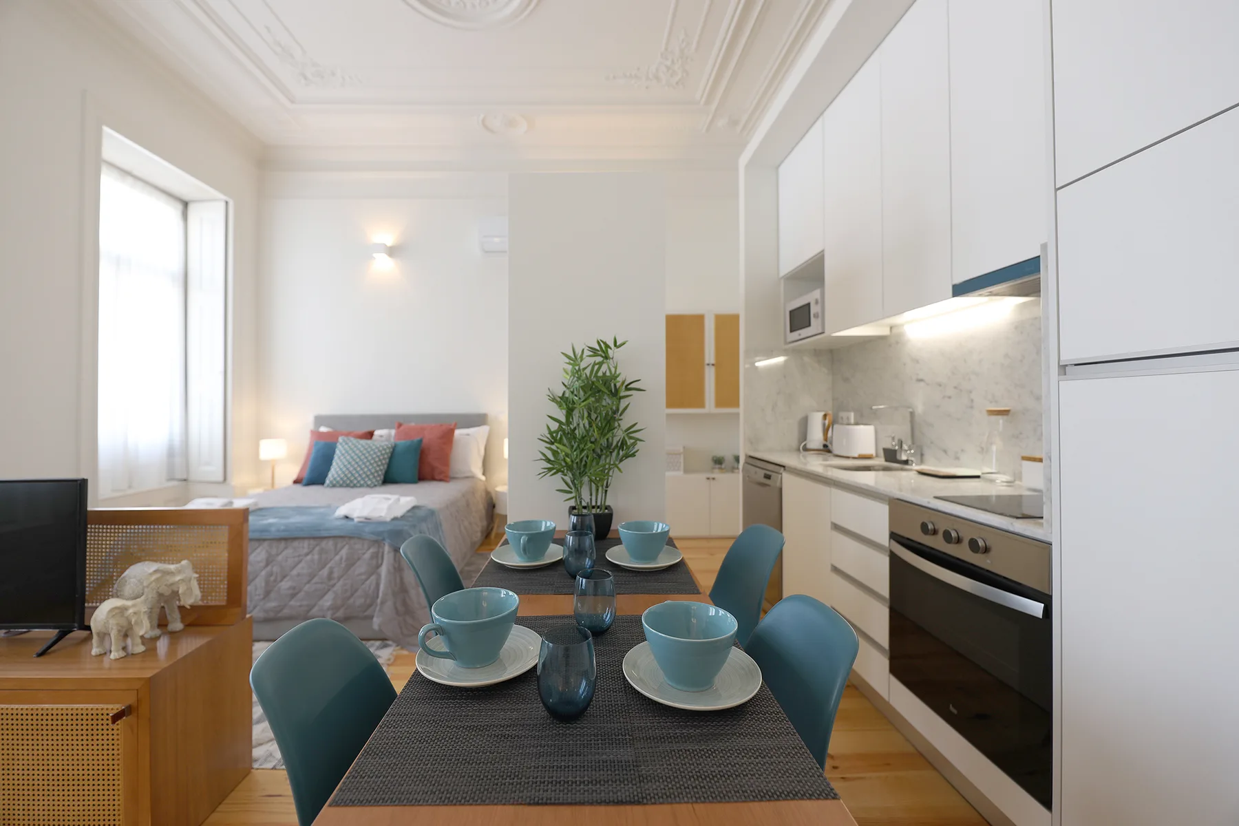 A studio combines a bed, dining table, and compact kitchen in one bright room.