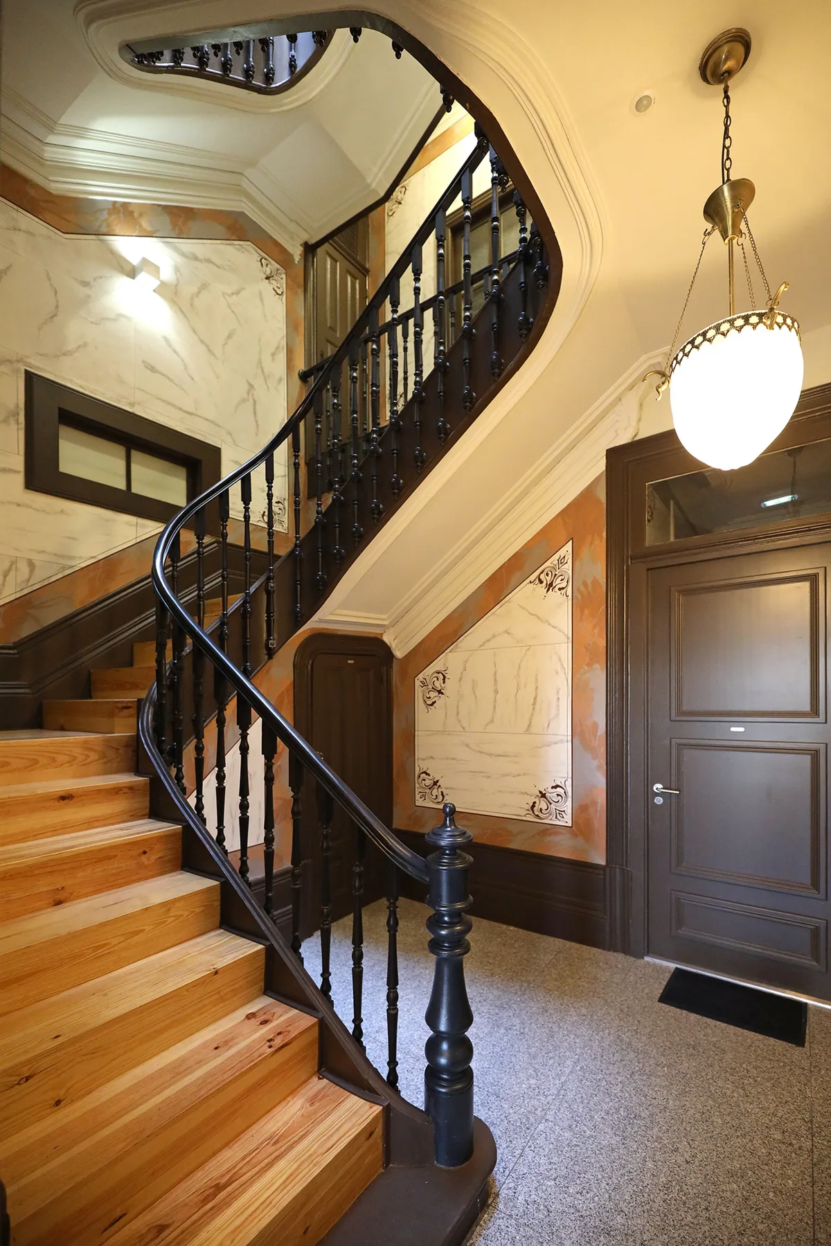 A curved staircase with wooden steps and dark railings fills this ornate interior.