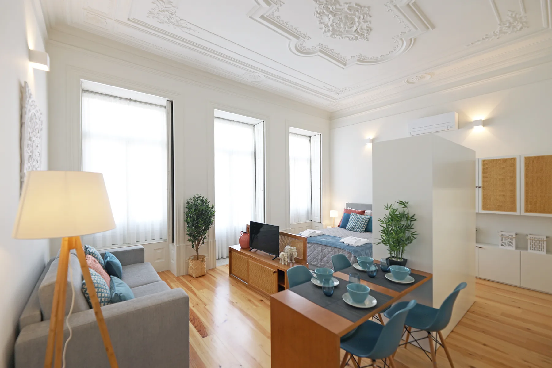 A bright studio living area with seating, a dining table, and tall windows.