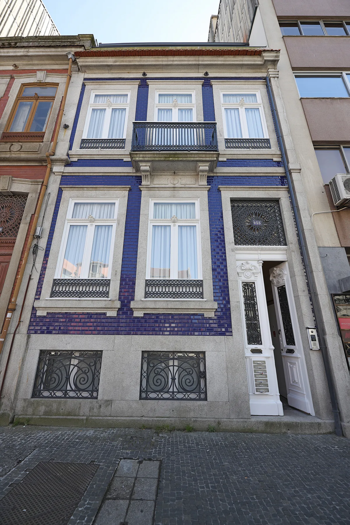 A narrow blue-and-white tiled building façade with tall windows and a street entrance.