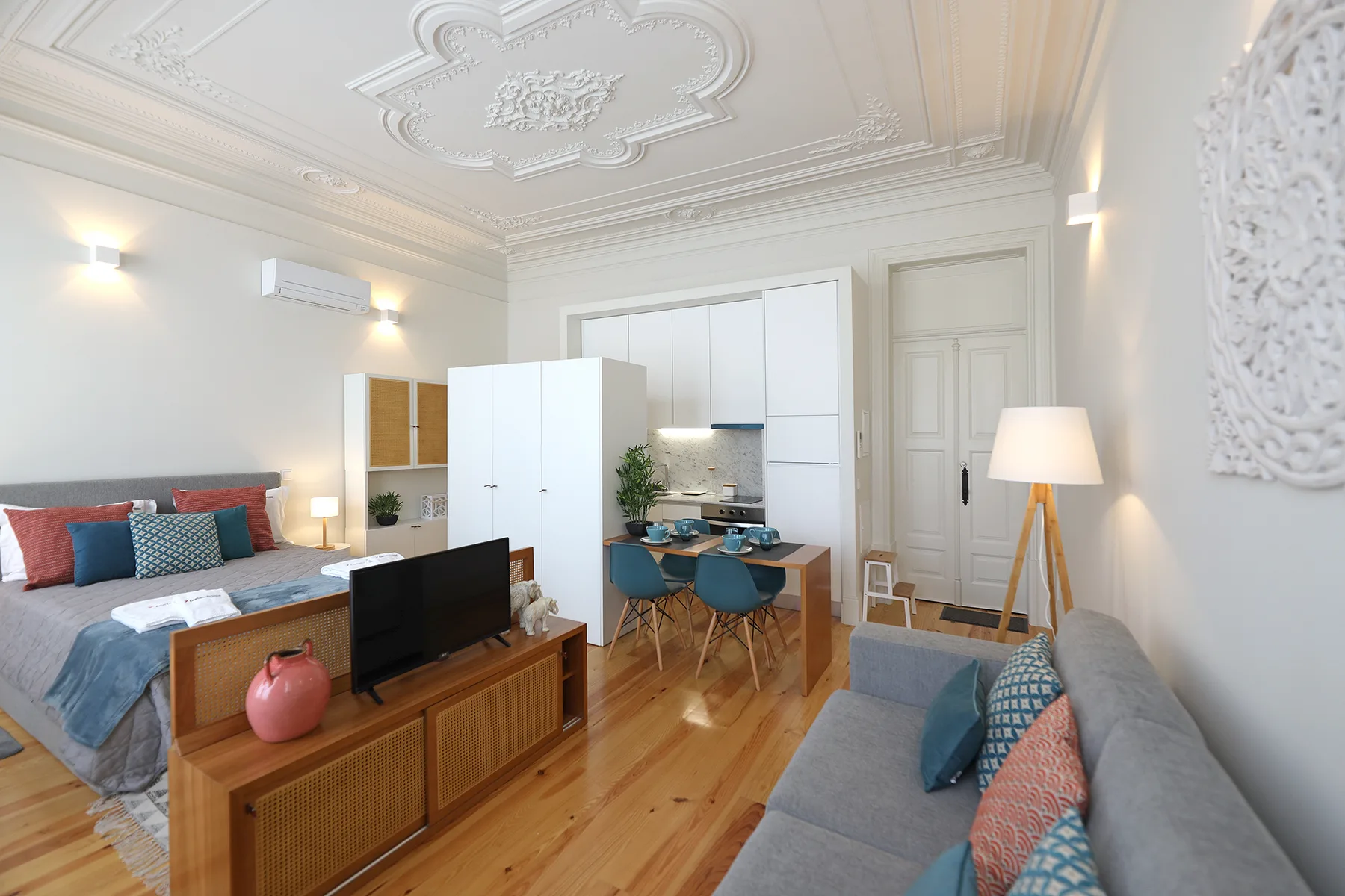 A bright studio living area with seating, a television, and a compact kitchen.