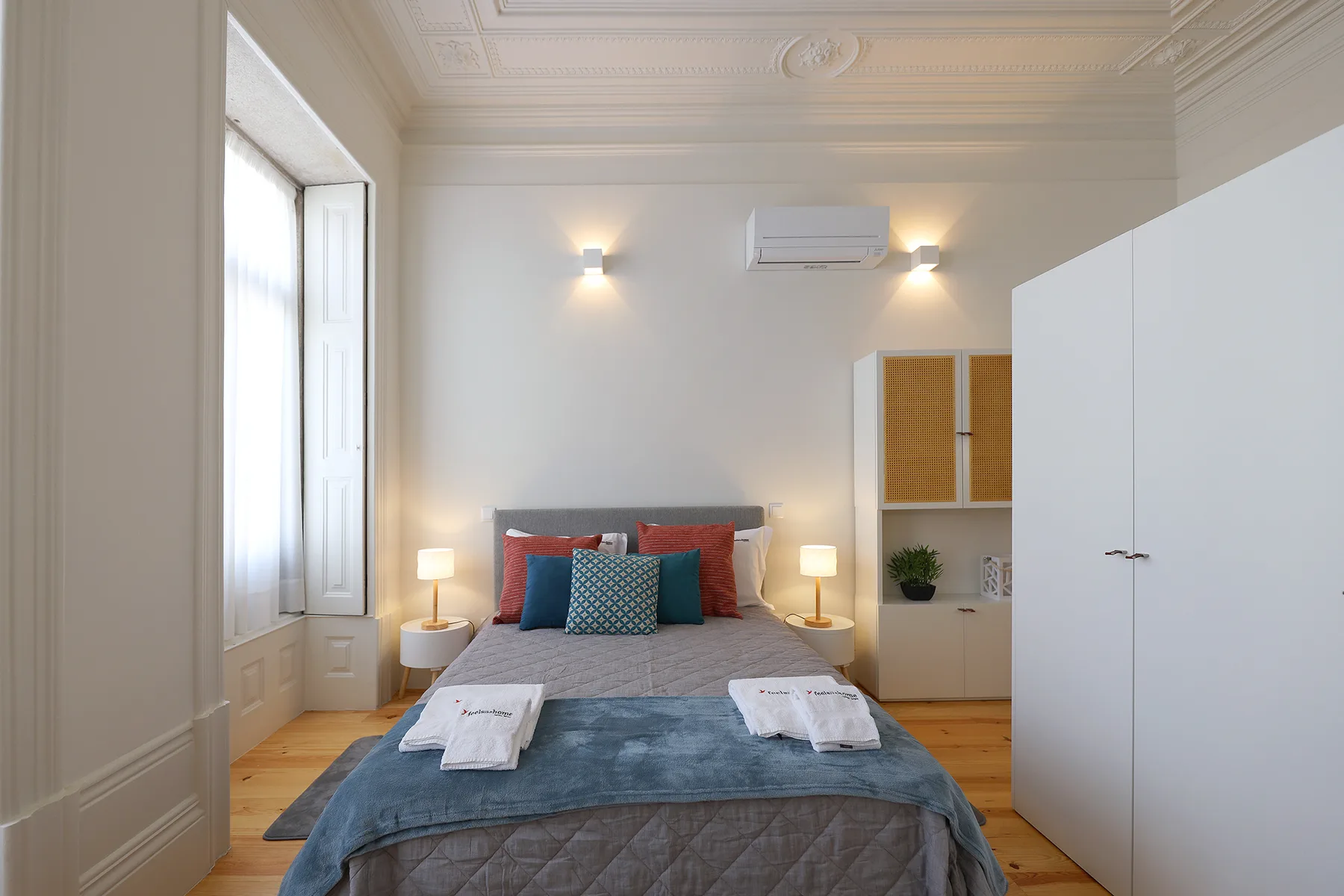 A bedroom with a neatly made bed, bedside lamps, and tall windows.