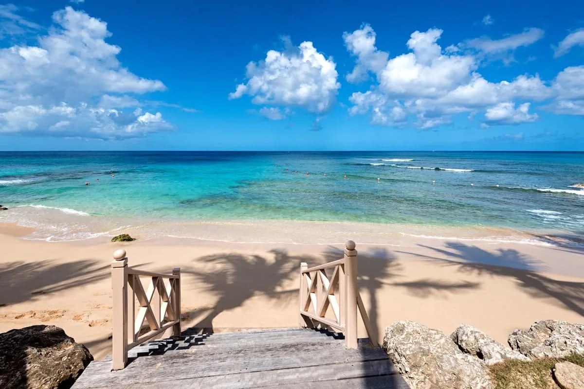 A wooden beach access walkway opens onto a sandy shore and turquoise water.