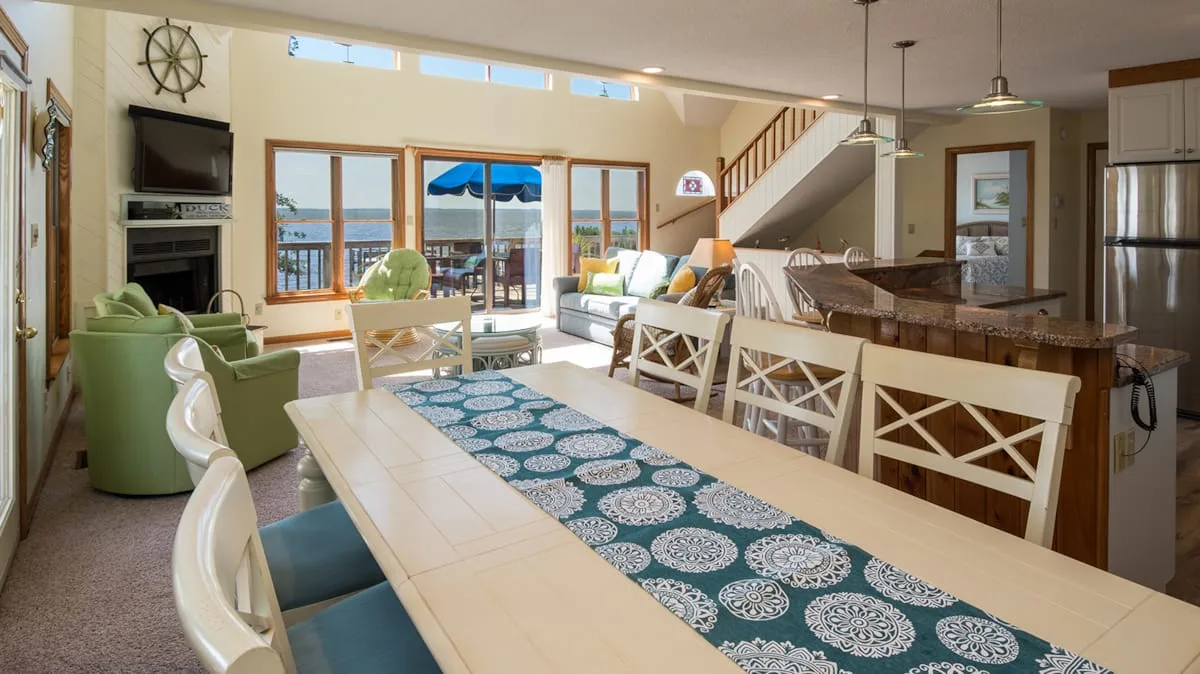 Una luminosa sala-comedor de concepto abierto con una mesa larga junto a grandes ventanas.