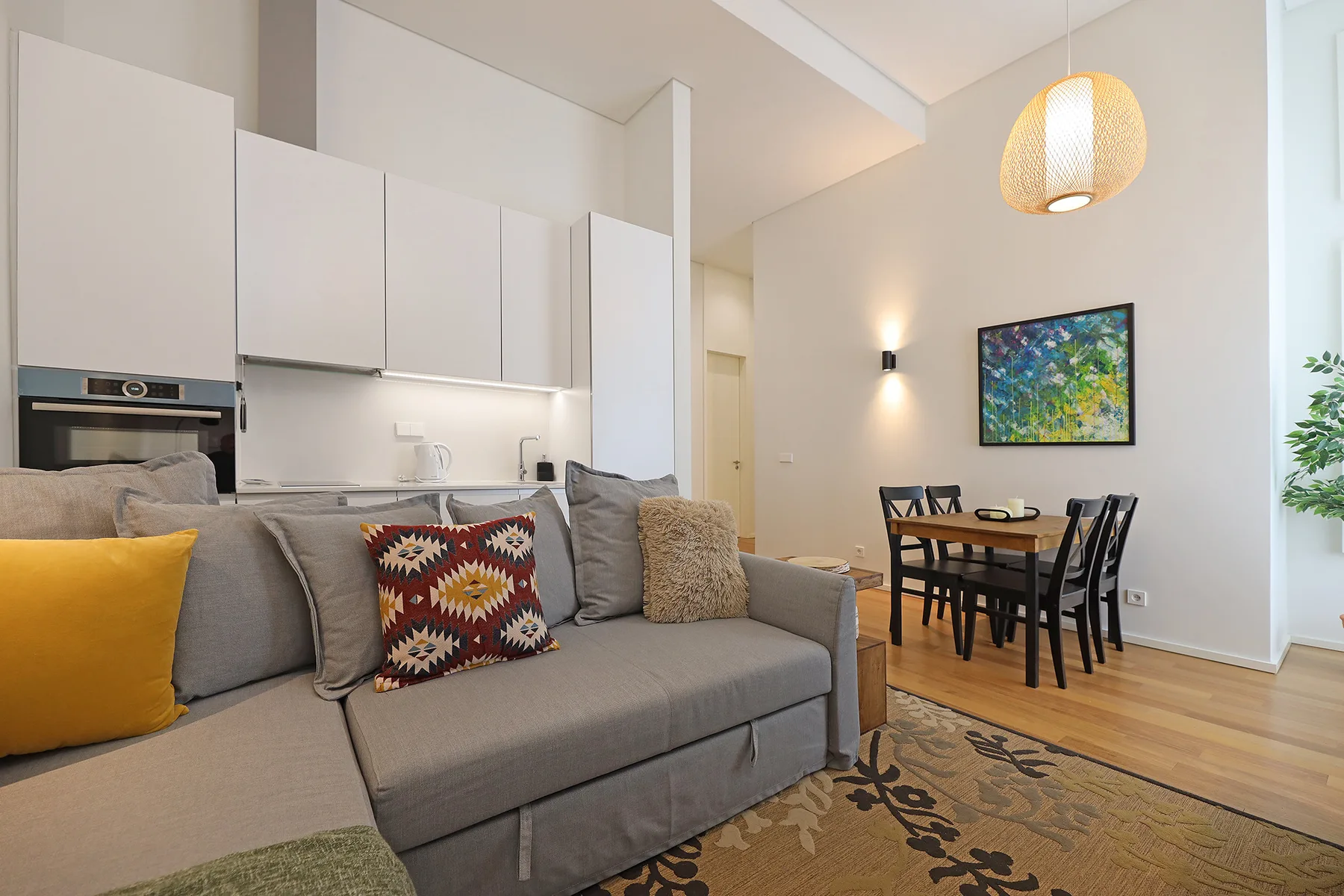 A living and dining area with gray seating, a kitchen, and a table.
