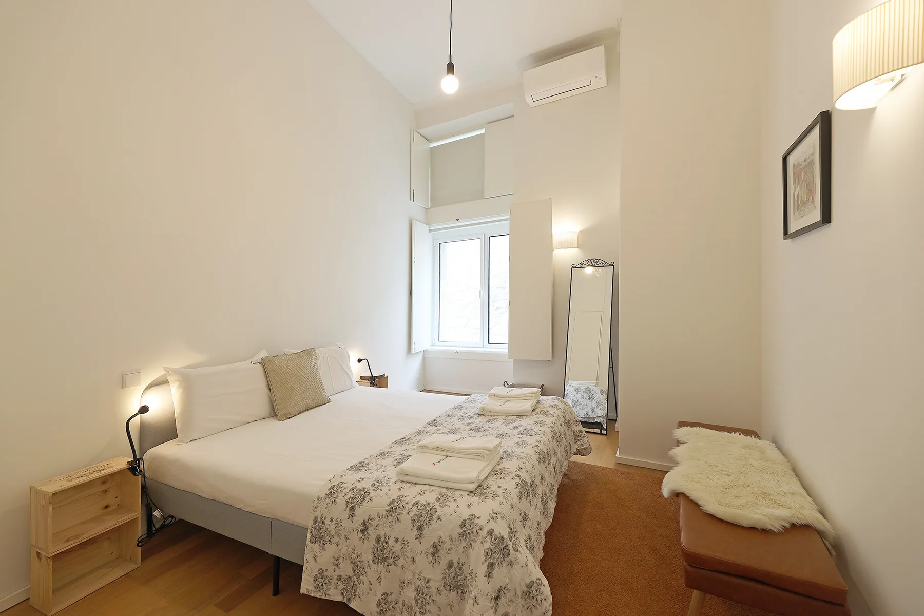 A bright bedroom with a double bed, patterned bedding, and a window.