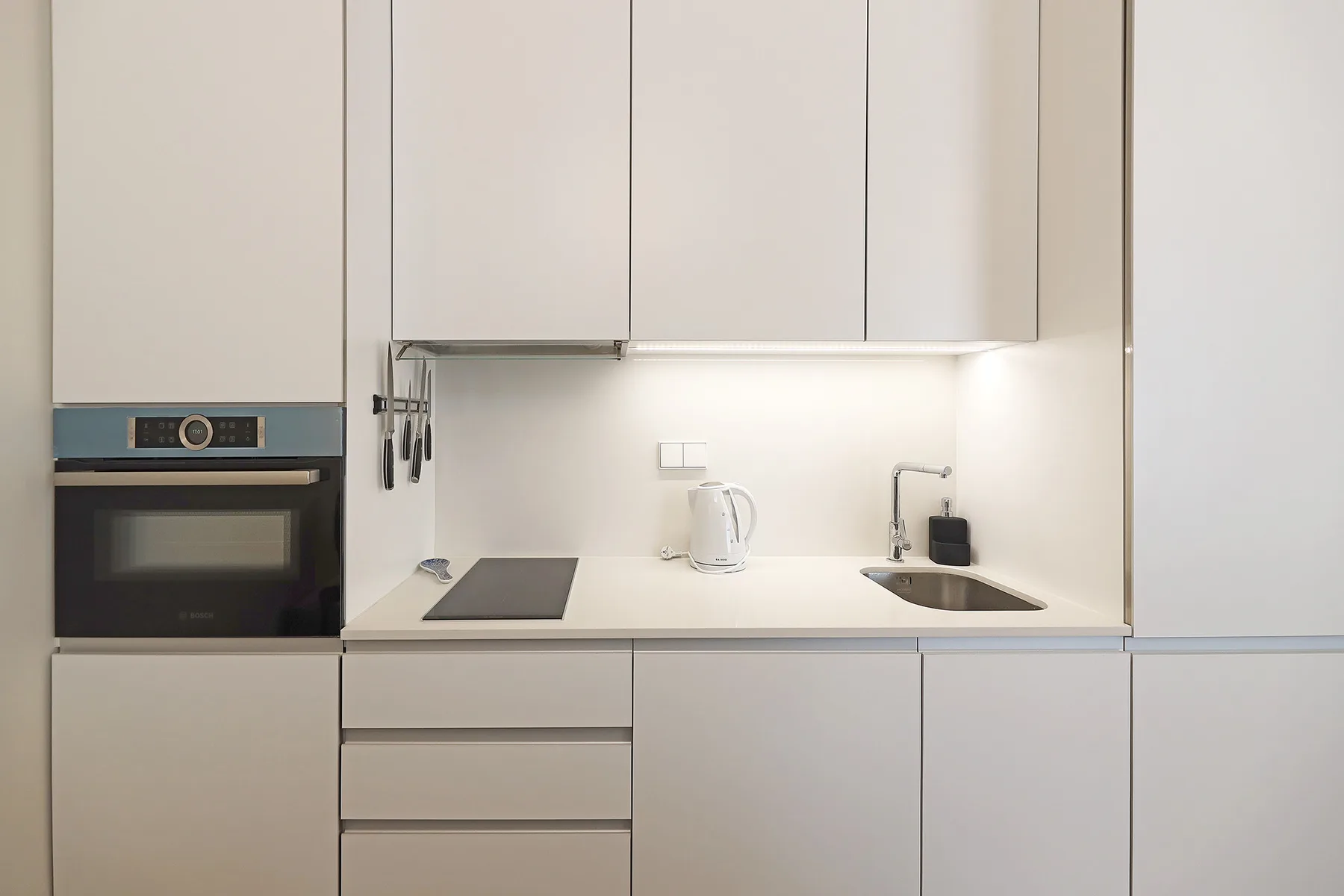 A modern kitchen with white cabinets, a cooktop, oven, and sink.