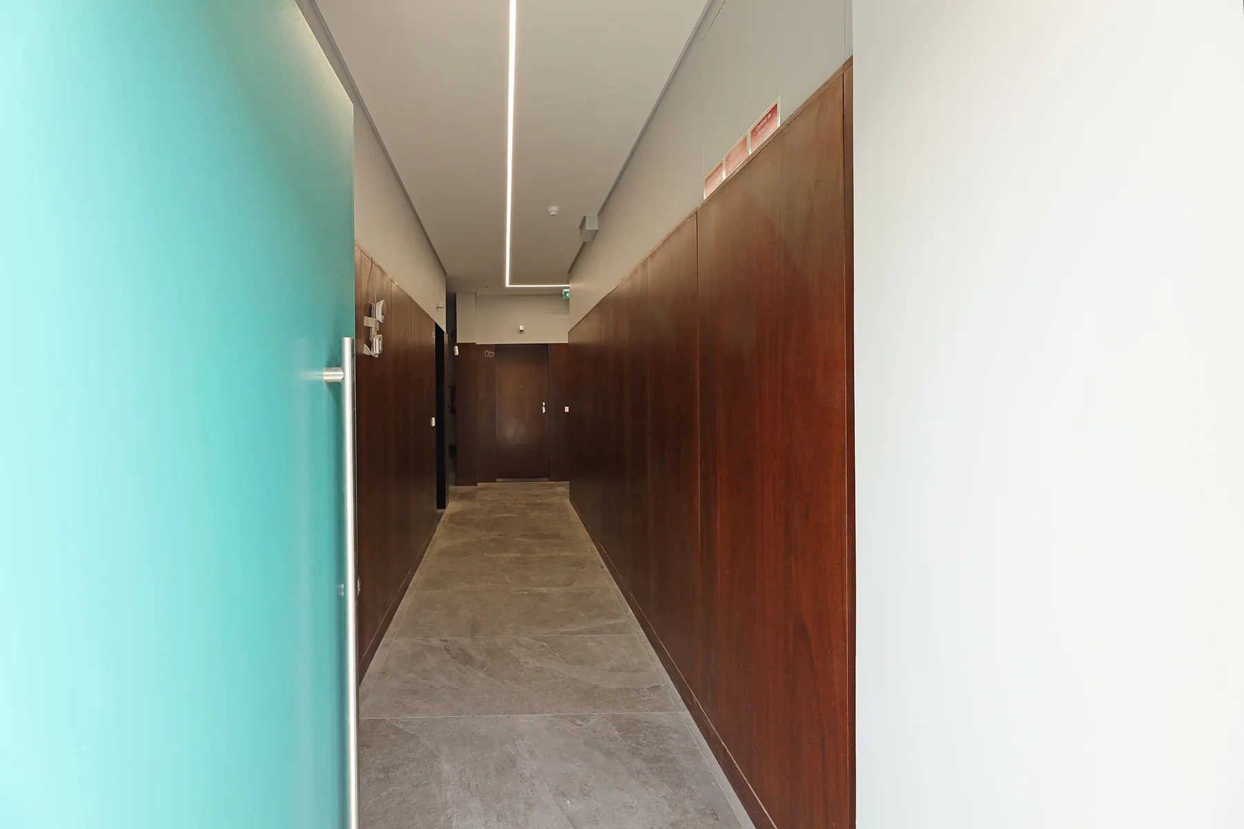 A narrow hallway with wood-paneled walls and a gray tiled floor.