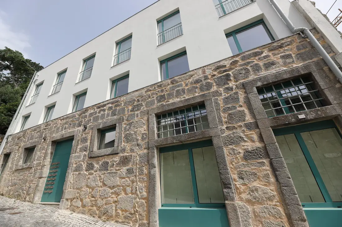 A white building rises above a stone facade with teal-framed windows.
